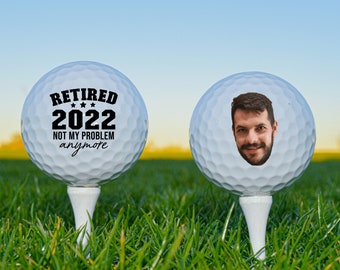 May include: Two white golf balls, one with the text "Retired 2022 Not My Problem anymore" and the other with a photo of a man's face.