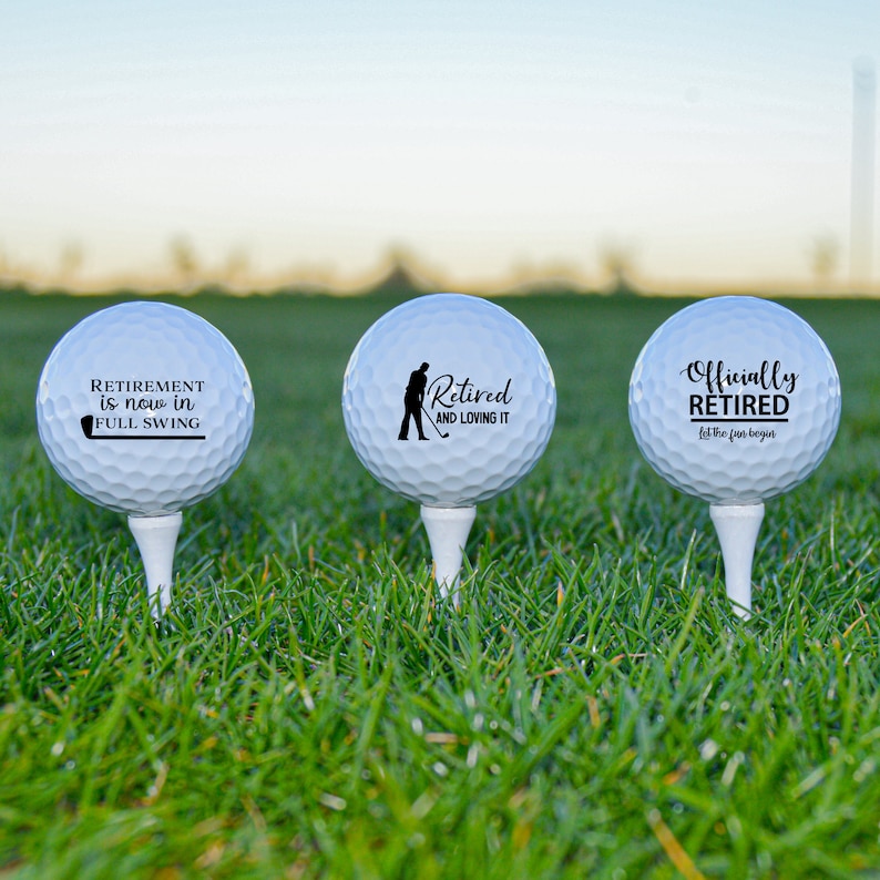 Pode incluir: Tr&ecirc;s bolas de golfe brancas com texto preto e uma silhueta de um golfista. O texto nas bolas diz "Retirement is now in full swing", "Retired and loving it" e "Officially Retired let the fun begin".