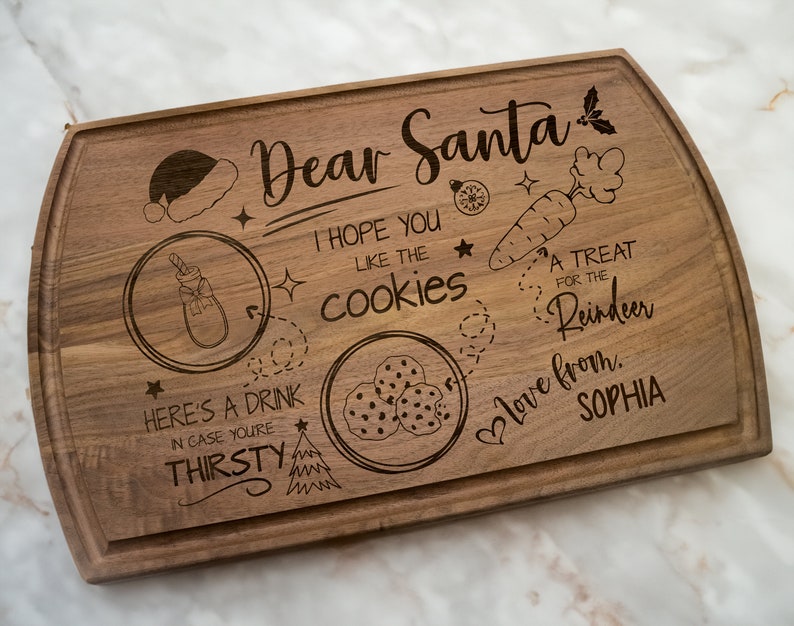 May include: A wooden cutting board with a Christmas-themed design. It says "Dear Santa, I hope you like the cookies. A treat for the reindeer. Love from, Sophia".