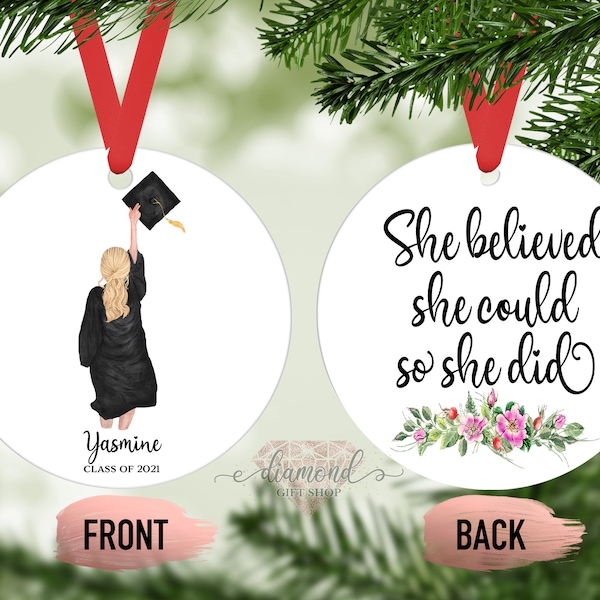Pode incluir: Um ornamento redondo branco com um chapéu de formatura e uma mulher com uma beca de formatura preta. O texto "Yasmine Classe de 2021" está na frente. A parte de trás do ornamento tem o texto "Ela acreditou que podia, então ela fez" com flores rosa.
