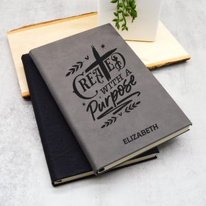 May include: Gray and black leather-bound journal with the text "Created with a Purpose" and a cross design. The name "Elizabeth" is printed on the bottom of the journal.