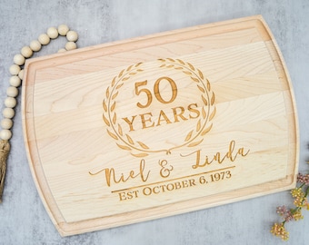 May include: A wooden cutting board with a personalized inscription celebrating a 50th anniversary. The inscription reads "50 Years Neil & Linda Est October 6, 1973".