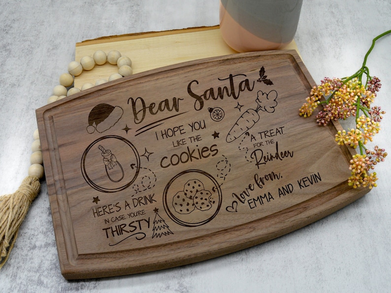 May include: A wooden cutting board with a Christmas-themed design. It says "Dear Santa, I hope you like the cookies. A treat for the reindeer. Love from Emma and Kevin."