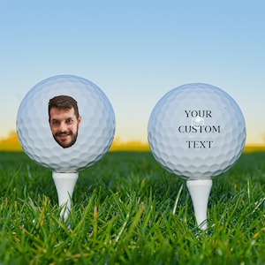 Pode incluir: Duas bolas de golfe brancas em grama verde. Uma bola tem o rosto de uma pessoa impresso nela. A outra bola tem o texto "YOUR CUSTOM TEXT" impresso nela.