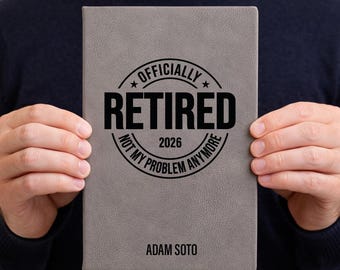 May include: A gray journal with the words "OFFICIALLY RETIRED 2026 NOT MY PROBLEM ANYMORE" in a black circular design. The name "ADAM SOTO" is printed below the text. The journal is held by a person.