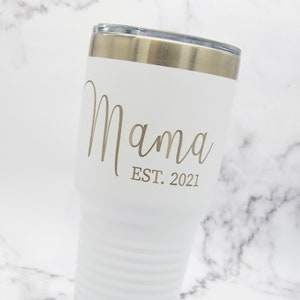 以下が含まれることがあります： 「ママ EST. 2021」と金色の文字で書かれた白いステンレス製のタンブラーです。