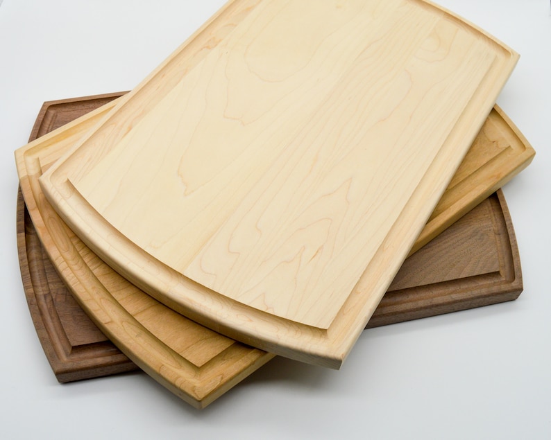 May include: Three wooden cutting boards, one brown and two light wood, with rounded edges and a decorative groove around the perimeter. The boards are stacked on top of each other.