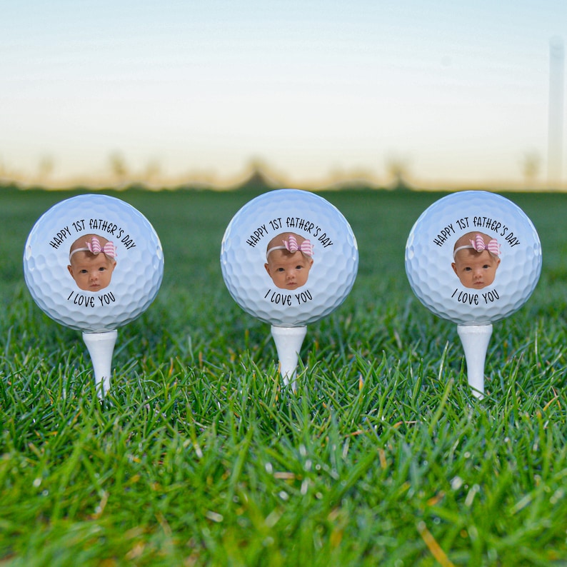 Pu&ograve; includere: Tre palline da golf bianche con il viso di un bambino e il testo "HAPPY 1ST FATHER'S DAY I LOVE YOU" su ogni pallina.