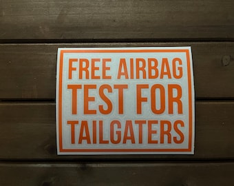 May include: A rectangular sticker with a white background and an orange border. The sticker has the words "FREE AIRBAG TEST FOR TAILGATERS" in bold orange letters.