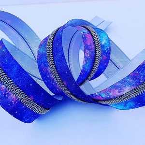 Puede incluir: Una cremallera azul y morada con estampado de galaxia. La cremallera tiene un deslizador de metal plateado y es perfecta para agregar un toque &uacute;nico a cualquier proyecto.