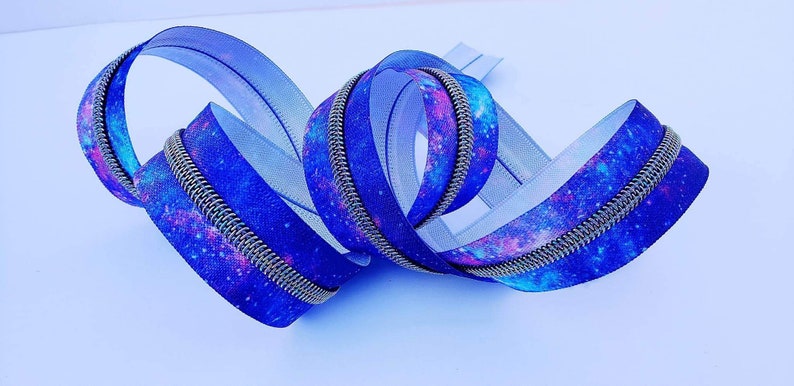 Puede incluir: Una cremallera azul y morada con estampado de galaxia. La cremallera tiene un deslizador de metal plateado y es perfecta para agregar un toque &uacute;nico a cualquier proyecto.