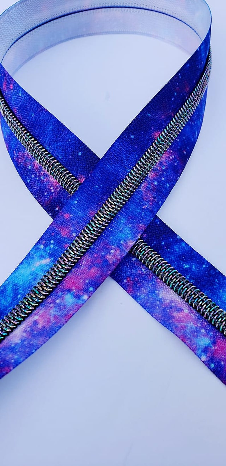 Puede incluir: Una cremallera con estampado de galaxia. La cremallera es azul, rosa y blanca con un tirador de cremallera plateado.