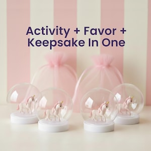 Puede incluir: Cuatro globos de nieve transparentes con base blanca y una figura de unicornio en su interior. Los unicornios tienen crines rosas y cuernos dorados. El fondo incluye dos bolsas de tul rosas y una pared a rayas rosas y blancas. Texto: Actividad + Favor + Recuerdo en uno.
