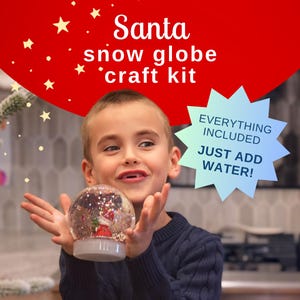 May include: A child holds a clear snow globe with a Santa Claus figurine inside. The snow globe is lit up and has a red base. The text "Santa snow globe craft kit" and "EVERYTHING INCLUDED JUST ADD WATER!" is visible in the image.