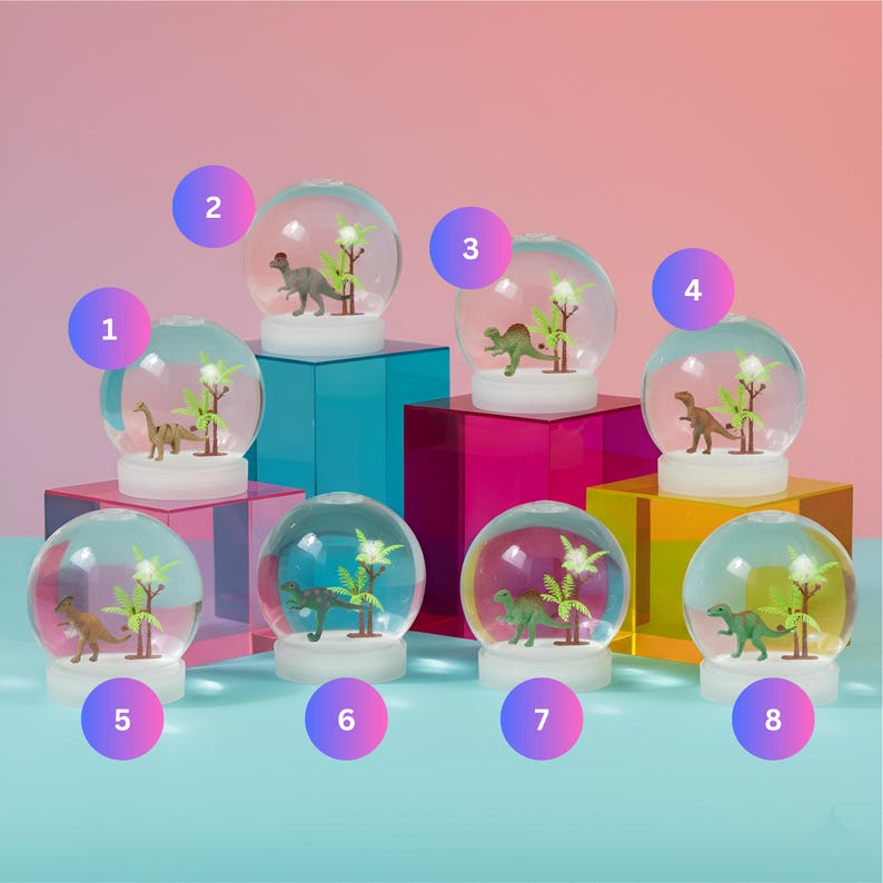May include: A collection of eight dinosaur-themed snow globes. Each globe features a miniature dinosaur figure and artificial plants inside a clear, spherical glass enclosure. The globes sit on colorful, geometric display blocks.