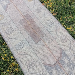 Pode incluir: Um tapete passadeira longo e retangular com um padrão desbotado e desgastado em tons de azul suave, rosa claro e creme. O design inclui um motivo de medalhão central rodeado por bordas florais intrincadas e linhas geométricas por toda a peça.