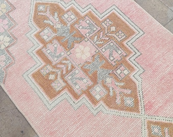 May include: A rectangular, vintage-style rug with a soft pink background and intricate geometric patterns in shades of brown, gray, and pink. The rug features a central medallion design and a border with floral motifs, suitable for home decor.