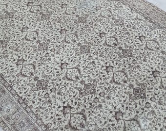 May include: A vintage cream-colored rug with a brown floral pattern. The rug has a detailed border with a repeating pattern.