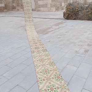 Puede incluir: Una alfombra larga y estrecha con un patrón floral en tonos de rosa, verde y amarillo. La alfombra está colocada sobre un suelo de baldosas grises.