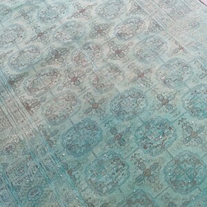 May include: A distressed, rectangular rug with a faded turquoise and brown color palette. The rug features a repeating geometric pattern with floral and medallion motifs. The rug's design has a vintage, antique aesthetic, suitable for home decor.