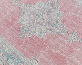 May include: A rectangular, distressed-look rug with a faded pink central field. The rug features a large, ornate central medallion in shades of blue, green, and cream. The border is a complementary blue-green with floral motifs.