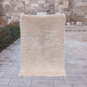 May include: A white shaggy rug with a long pile. The rug is displayed on a tiled floor.