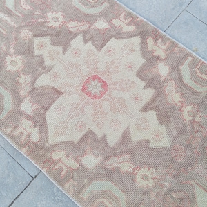 May include: A rectangular, vintage-style rug with a floral pattern in shades of beige, pink, and brown. The rug features a central medallion design and a border with repeating floral motifs. The rug is placed on a gray tiled floor.