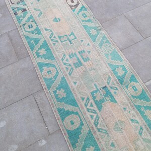 Peut inclure: Un tapis de couloir turquoise et crème avec un motif géométrique traditionnel. Le tapis a un aspect usé et vintage.
