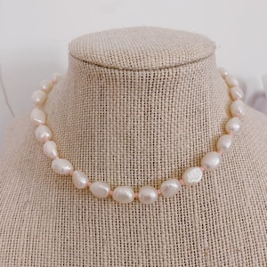 May include: A white pearl necklace with a pink thread strung through the pearls.