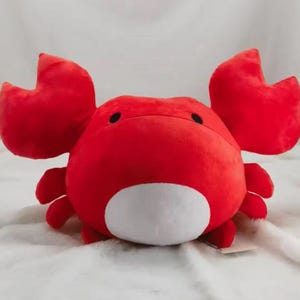 Pode incluir: Um brinquedo de pelúcia de caranguejo vermelho com grandes garras e barriga branca. O caranguejo tem pequenos olhos pretos e é feito de material macio. Este bicho de pelúcia é um brinquedo fofo e aconchegante.