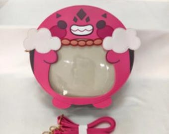 May include: A pink and black round purse with a cartoon character design. The purse has a clear plastic window and a pink adjustable strap.