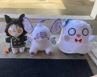 May include: Three plush toys in a row. The first is a cat-like creature in a black hooded outfit with orange accents. The second is a white creature with purple wings. The third is a white ghost-like figure with a red bow tie.