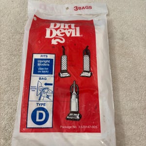 May include: A white packet of Dirt Devil vacuum cleaner bags. The packet features a red panel with the Dirt Devil logo and diagrams of upright vacuum cleaner models. The packet is labelled "Type D" and states it fits upright models.