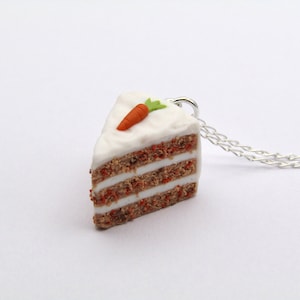 May include: A silver chain necklace with a carrot cake slice pendant. The cake is made of polymer clay and has a white icing with a green carrot on top.