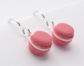 May include: A pair of silver dangle earrings featuring pink macarons with white frosting.