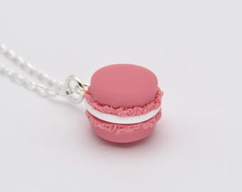 May include: A pink macaron with white filling on a silver chain necklace. The macaron is a popular French pastry.
