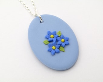 May include: A light blue oval pendant necklace with a cluster of three blue flowers with yellow centers and green leaves.