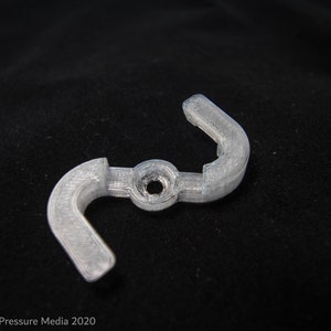 May include: A clear plastic 3D printed part with two curved arms and a central hole. The part is designed to be used as a connector or a bracket.