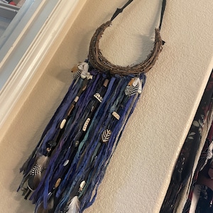May include: A blue and brown dreamcatcher with feathers and beads hanging from a woven hoop. The dreamcatcher is hanging from a black cord.
