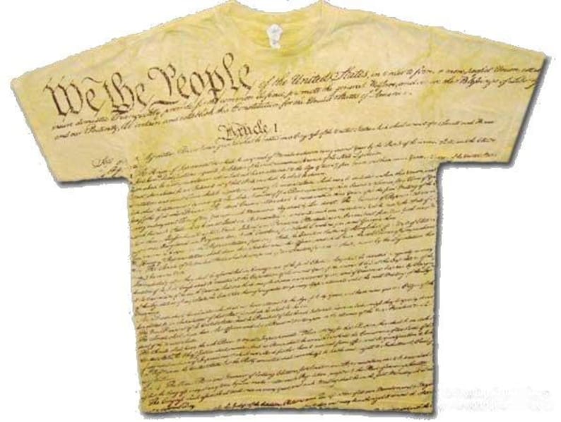 Pu&ograve; includere: Una maglietta gialla con il testo completo della Costituzione degli Stati Uniti stampato su di essa. Il testo &egrave; in inchiostro marrone e le parole "We the People" sono stampate in un carattere pi&ugrave; grande nella parte superiore della maglietta.