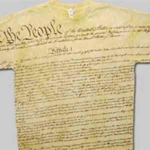 Pu&ograve; includere: Una maglietta gialla con il testo "We the People" stampato sul davanti. L'intero testo della Costituzione degli Stati Uniti &egrave; stampato sulla maglietta in un font in stile vintage.