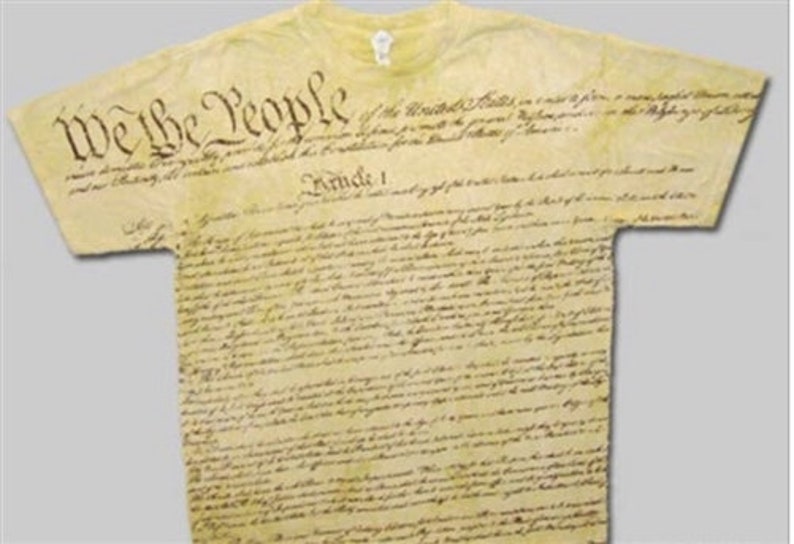 Pu&ograve; includere: Una maglietta gialla con il testo "We the People" stampato sul davanti. L'intero testo della Costituzione degli Stati Uniti &egrave; stampato sulla maglietta in un font in stile vintage.