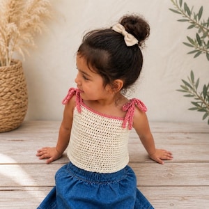 May include: A cream-colored crochet top with pink trim and straps, paired with a blue denim skirt. The top is worn by a young child. The text "Crochet Kids Top Pattern" is displayed at the bottom of the image.