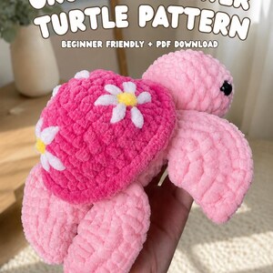 May include: A plush crochet turtle toy with a bright pink shell decorated with white and yellow flower appliques and a light pink head and flippers. The text CROCHET FLOWER TURTLE PATTERN BEGINNER FRIENDLY + PDF DOWNLOAD is visible above the toy.