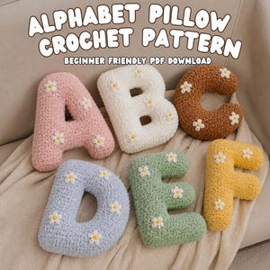 Könnte beinhalten: Ein Set aus sechs weichen Alphabet-Kissen in Form der Buchstaben A, B, C, D, E und F. Jedes Kissen ist in Pastellfarben wie Rosa, Weiß, Braun, Blau, Grün und Gelb gehäkelt und mit kleinen, aufgesetzten weißen Gänseblümchen verziert.