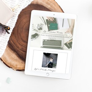 May include: A white tablet computer displaying a website with the text "La Femme Forte" and "Let's Make Magic". The website features a photo of a laptop computer with a green notebook and a glass of water. The website also features a photo of a person standing in front of a wall.