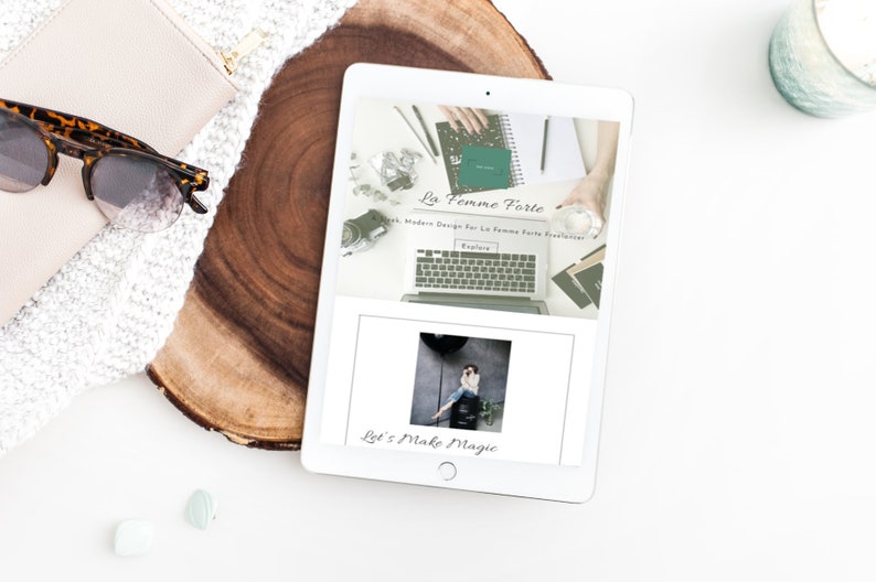 May include: A white tablet computer displaying a website with the text "La Femme Forte" and "Let's Make Magic". The website features a photo of a laptop computer with a green notebook and a glass of water. The website also features a photo of a person standing in front of a wall.