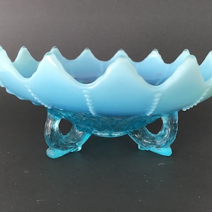 May include: A light blue glass bowl with a scalloped edge and three legs. The bowl has a frosted finish and is decorated with small dots.