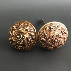 Puede incluir: Dos pomos de puerta dorados adornados con intrincados diseños florales.