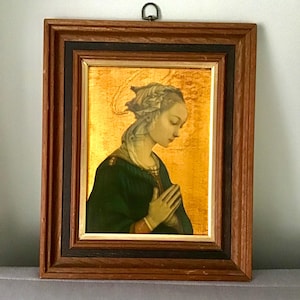 Könnte beinhalten: Ein gerahmter Druck einer Frau mit Heiligenschein, die ein grünes Gewand trägt und mit gefalteten Händen betet. Der Hintergrund ist golden.